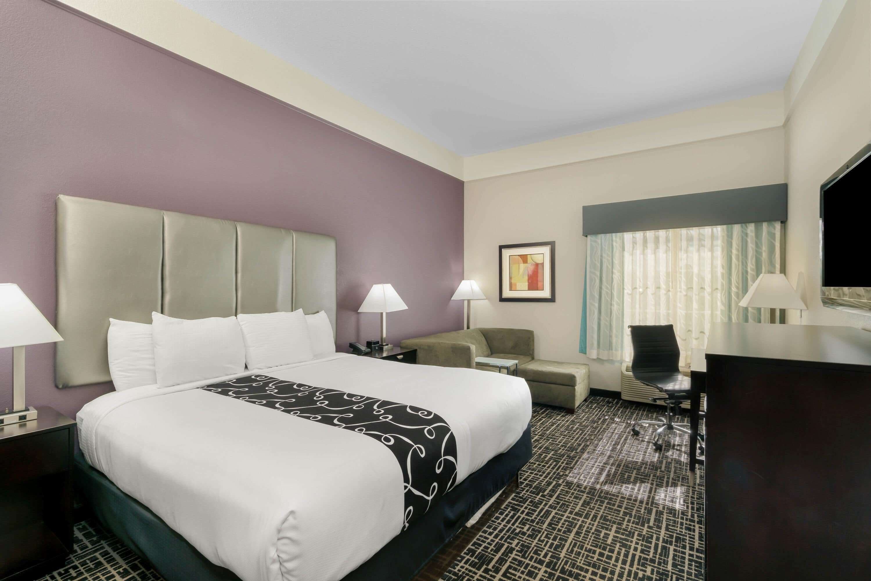 A hotel room with a large bed, two bedside tables with lamps, a desk with a chair, a sofa, and a TV.