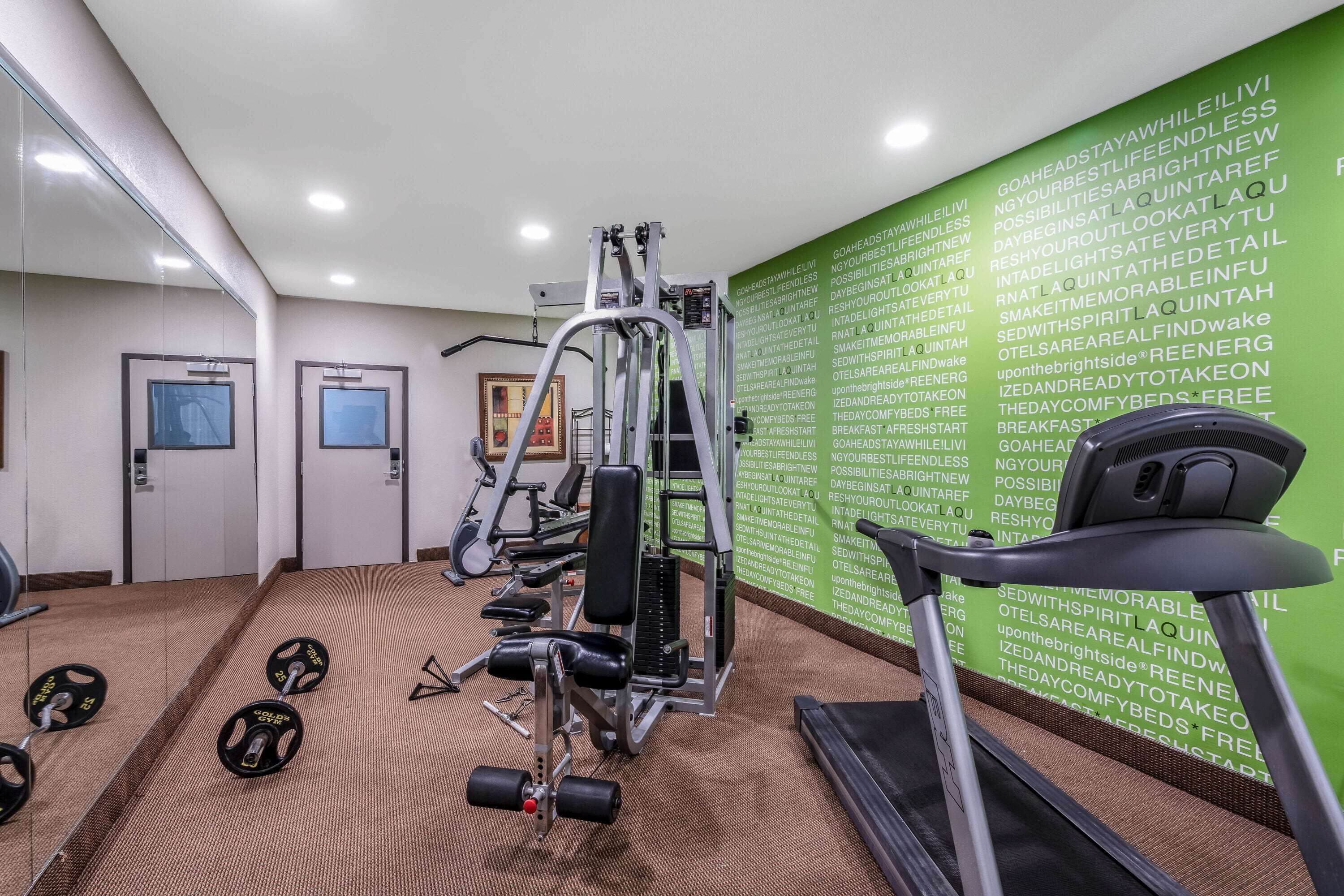A gym with weightlifting equipment, a treadmill, and a wall with motivational text.