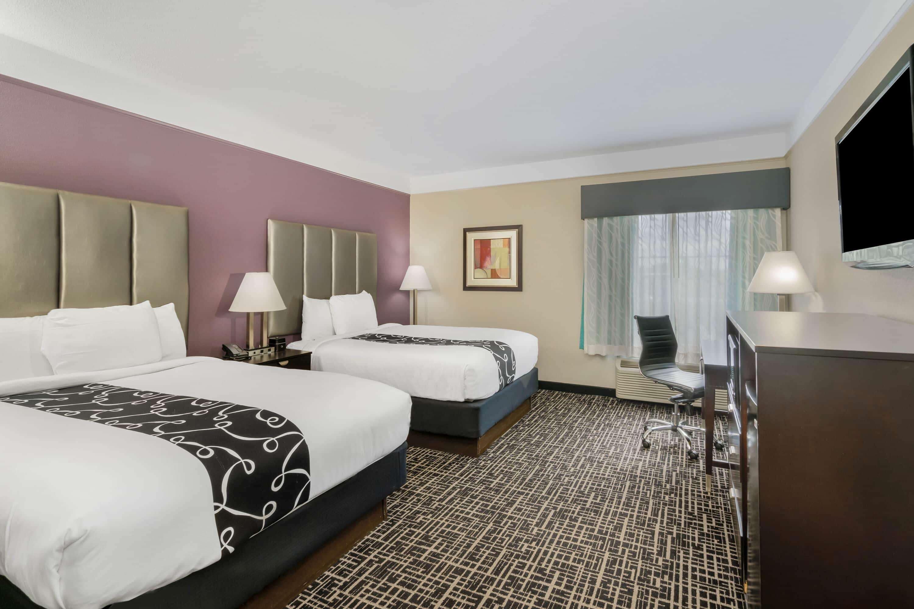 A hotel room with two beds, a desk, a chair, a TV, and a window with curtains.