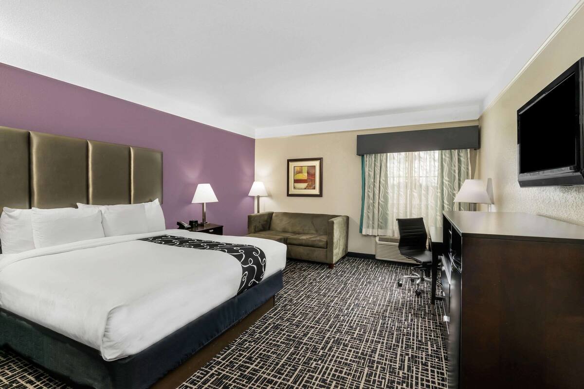 A hotel room with a large bed, a desk, a chair, a sofa, and a television.