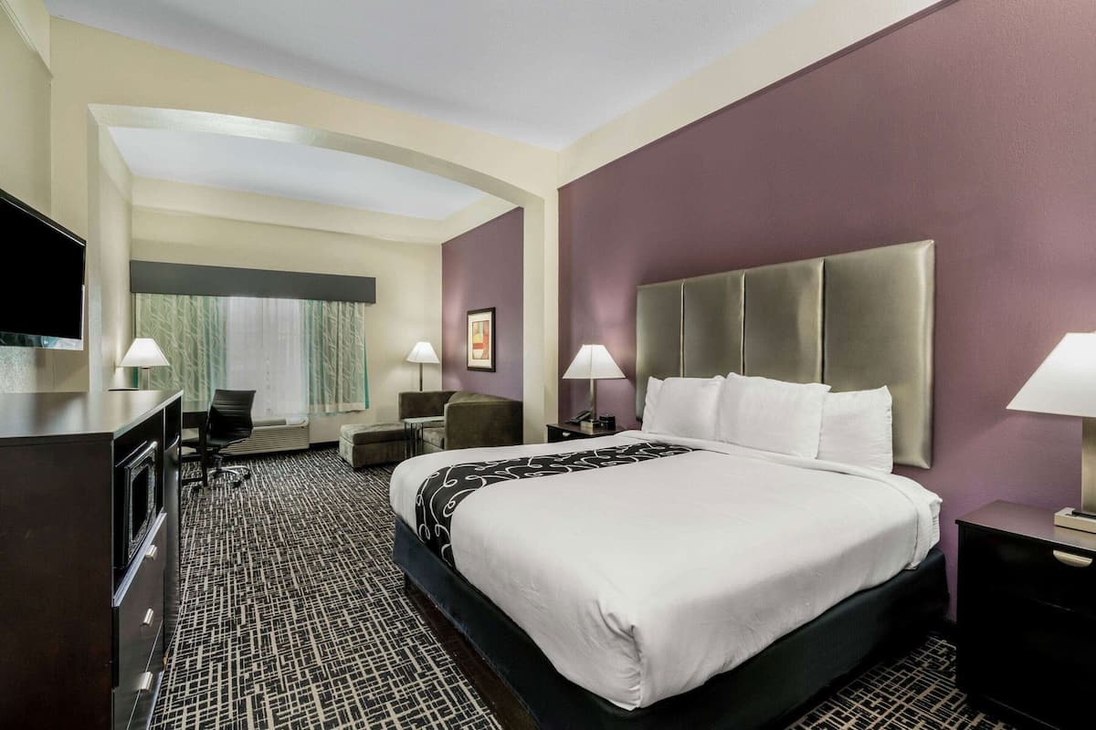 A hotel room with a large bed, a desk, a chair, a TV, and a window with curtains.