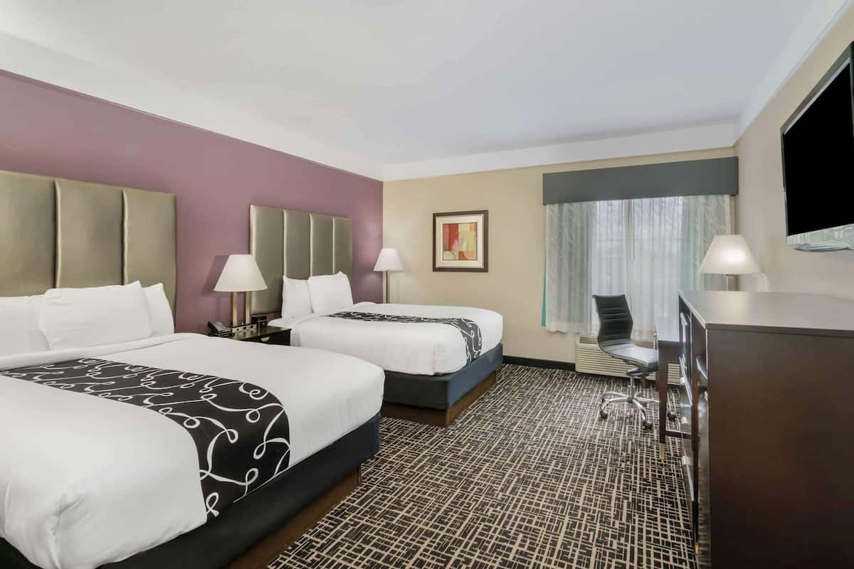 A hotel room with two beds, a desk, a chair, and a television.