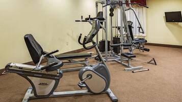 Un gimnasio con diversas máquinas de ejercicio, un televisor montado en la pared y suelo cubierto de alfombra.