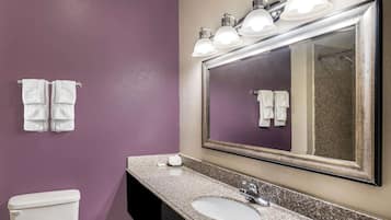 A bathroom with a purple wall, a white toilet, a sink with a mirror above it, and two towels hanging on the wall.