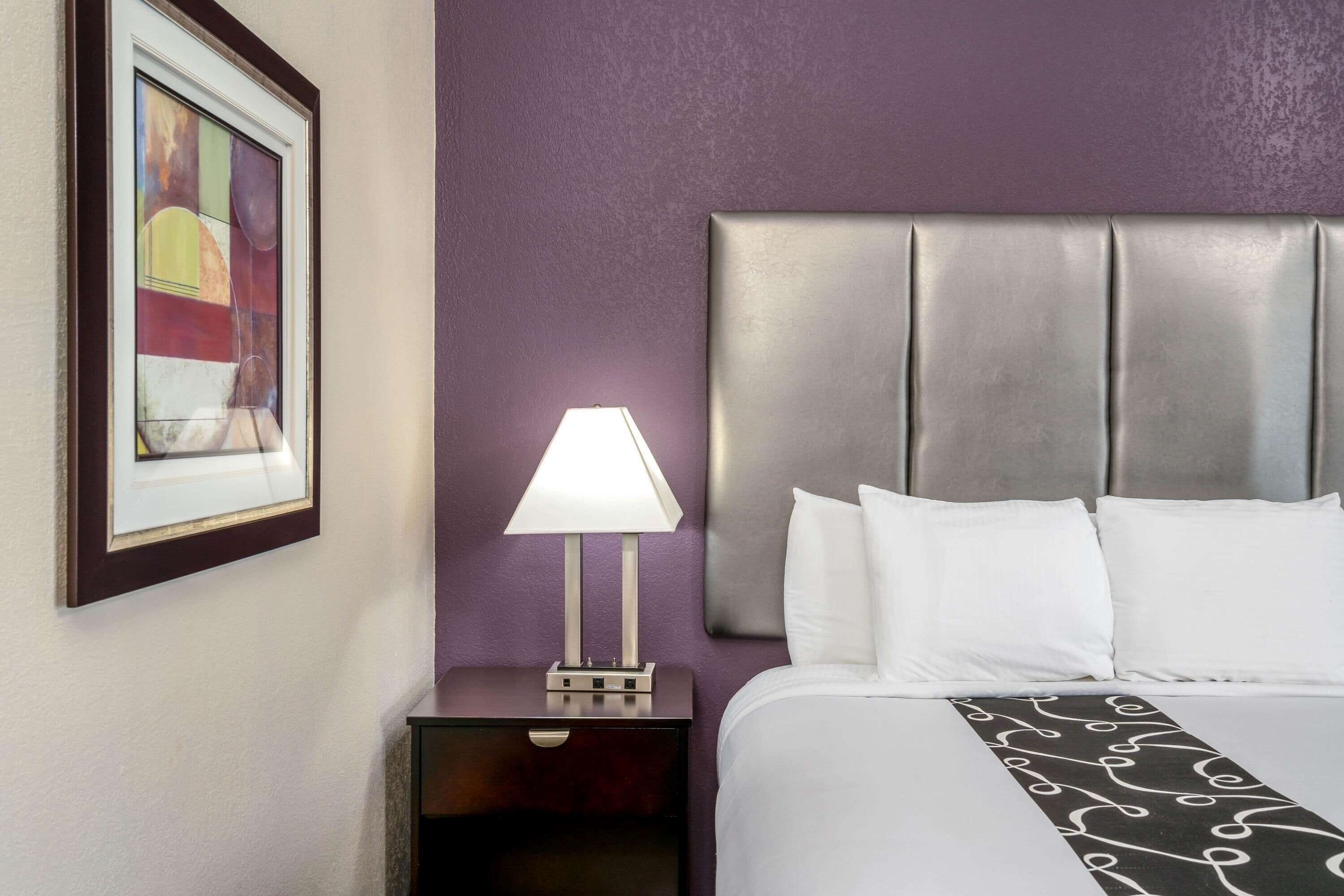 Una habitación de hotel con una cama, una mesita de noche con lámpara y una obra de arte enmarcada en la pared.