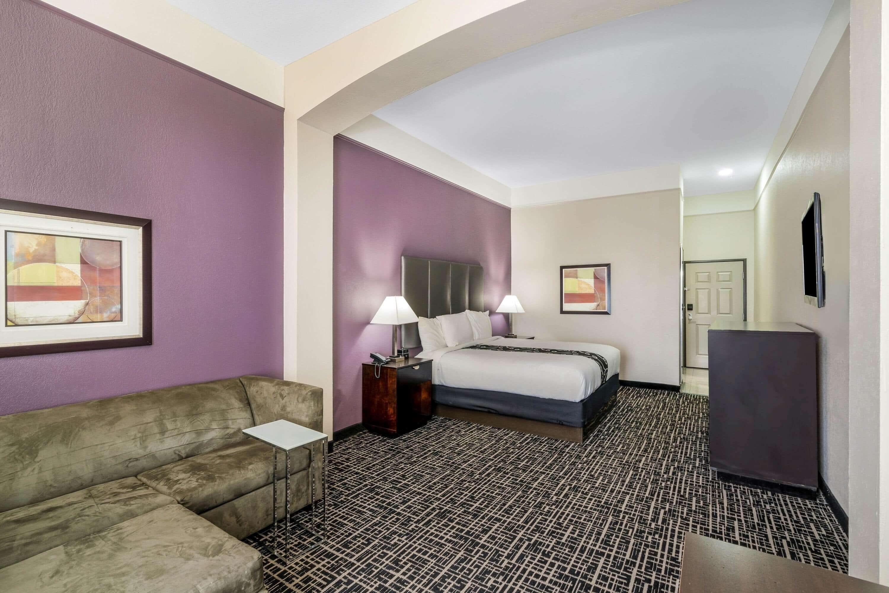 Een hotelkamer met een bed, twee bedlampen, een nachtkastje, een bank, een televisie en een kamerbreed tapijt met een patroon.