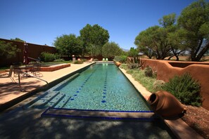 Ein rechteckiger Pool mit klarem, blauem Wasser, umgeben von einem angelegten Garten mit Bäumen und Sträuchern.