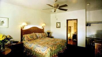A bedroom with a bed, two bedside lamps, a ceiling fan, a framed picture on the wall, and a mirror on the door.