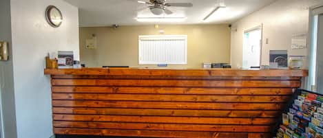 A reception desk with a wooden finish, a ceiling fan, a clock, and a window with blinds.