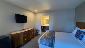 Une chambre à coucher avec un lit, une commode, un téléviseur et une salle de bain visible à travers une porte ouverte.