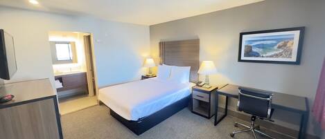 Habitación de hotel con cama, mesitas de noche, un escritorio con silla, televisión y un cuadro en la pared.