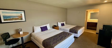 A hotel room with two beds, a desk, a chair, a small table with a menu, and a framed picture on the wall.