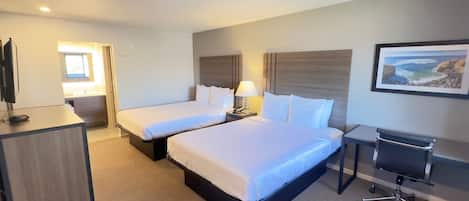 Quarto de hotel com duas camas, uma escrivaninha, uma cadeira, uma televisão e um quadro na parede.
