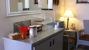 Una recepción de hotel con una cafetera, una vitrina de vidrio con pasteles y una lámpara.