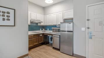 Una cocina compacta con gabinetes blancos, un refrigerador de acero inoxidable y un salpicadero de azulejos azules.