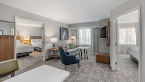 A hotel room with a bed, a sofa, a chair, a small table, and a TV.