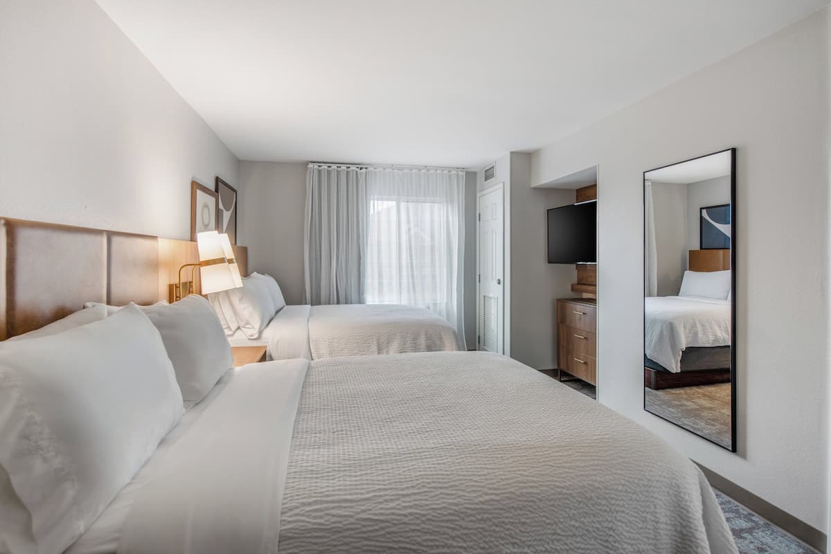 A hotel room with two beds, a TV, a wardrobe, and a large mirror.