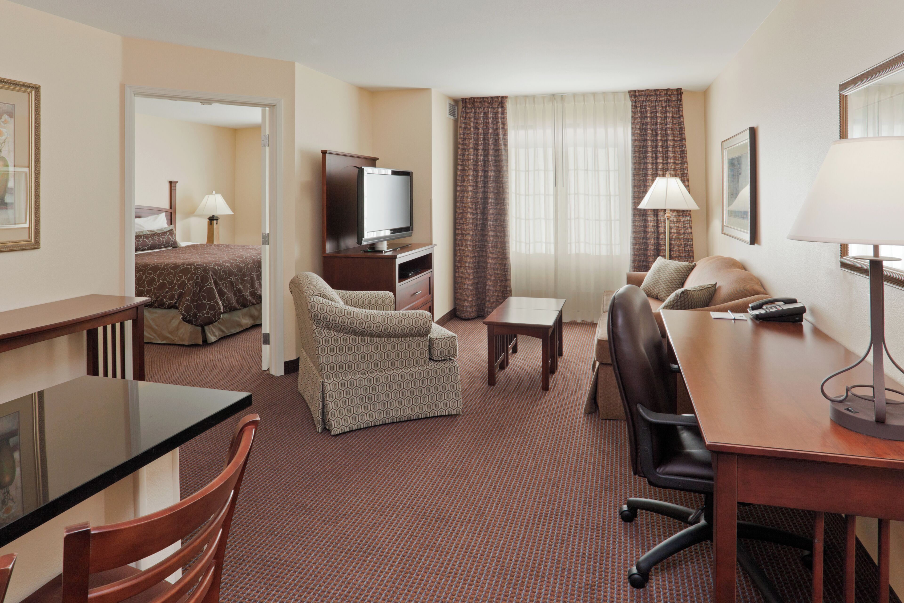 A hotel room with a bed, a TV, a desk, a chair, a sofa, and a lamp.