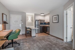 Eine moderne Küche mit weißen Schränken, einem Kühlschrank und einer Mikrowelle. Ein Essbereich mit einem grünen Stuhl und einem Tisch.