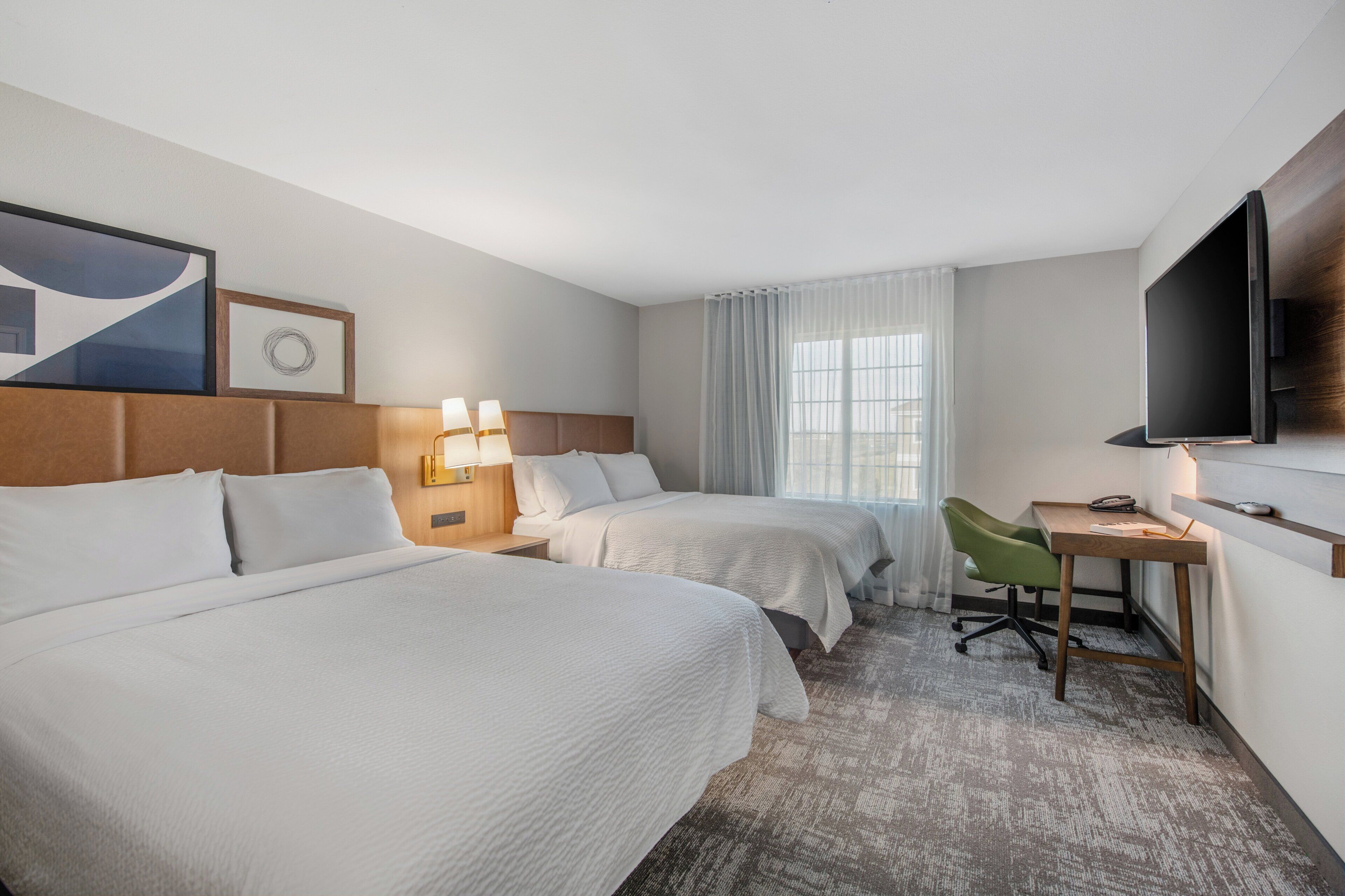 A hotel room with two beds, a desk, a chair, a TV, and a window with curtains.