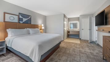 Una habitación de hotel moderna con una cama grande, televisión, escritorio y baño visible a través de una puerta abierta.