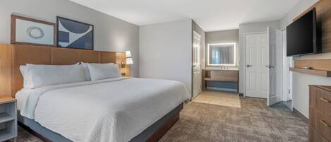 Una habitación de hotel moderna con una cama grande, televisión, escritorio y baño visible a través de una puerta abierta.