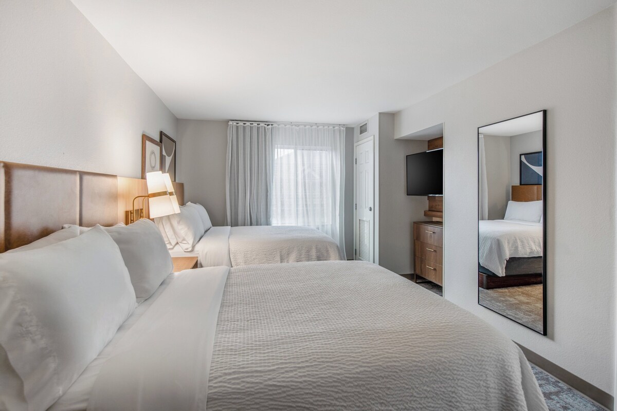 Ein Hotelzimmer mit zwei Betten, einem Fernseher, einem Kleiderschrank und einem großen Spiegel.