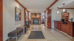 A hotel lobby with a stone fireplace, wooden benches, a reception desk, and a clock on the wall.
