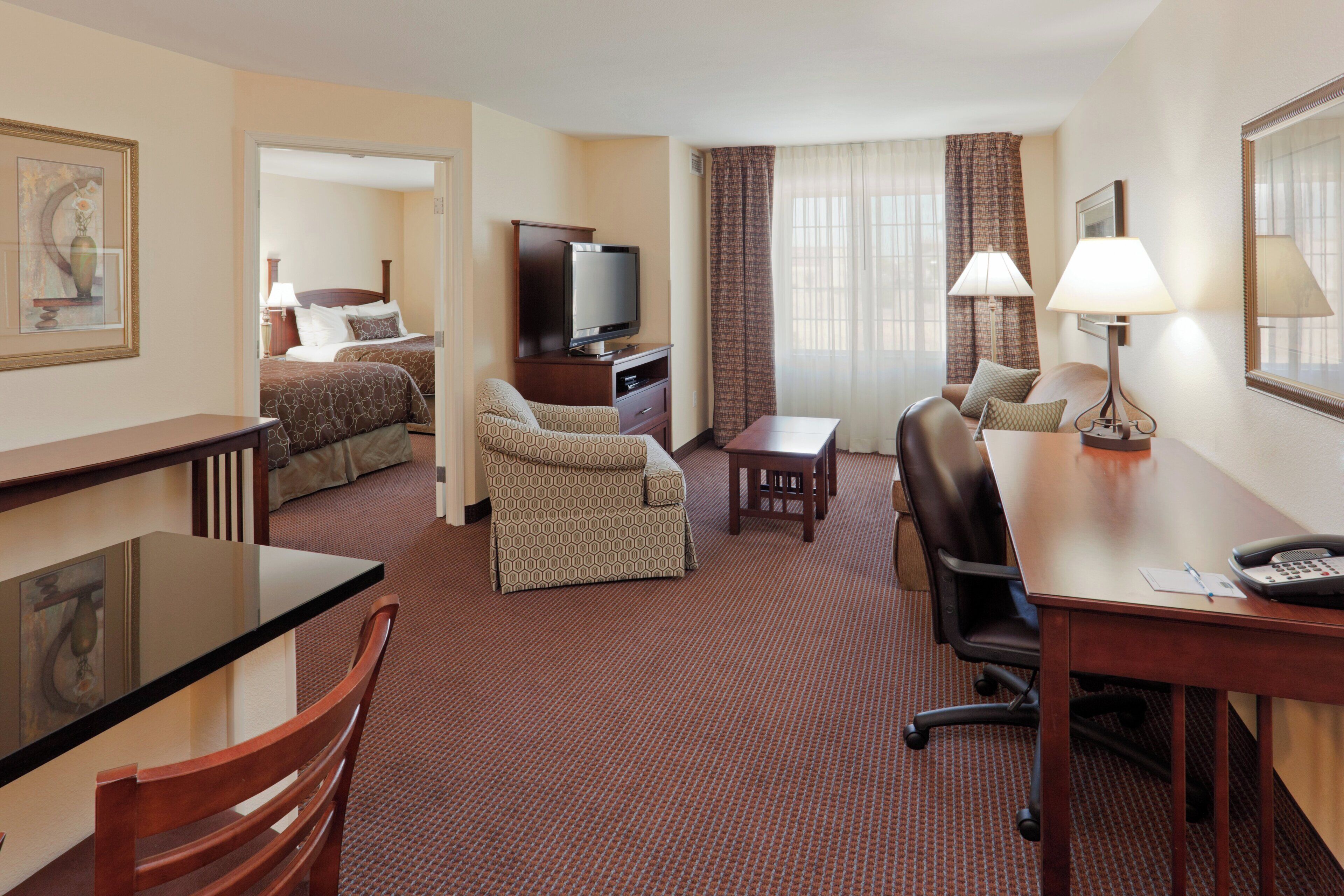 A hotel room with a bed, a desk, a chair, a television, and a lamp.
