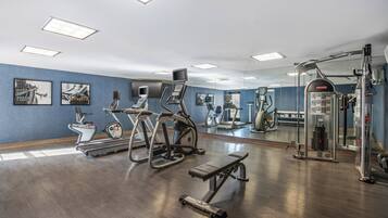 Un gimnasio con cintas de correr, elípticas, una prensa de banca y un espejo grande.