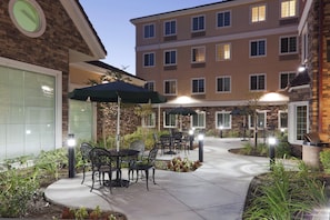 A courtyard with outdoor seating, a brick building, and a multi-story structure in the background.