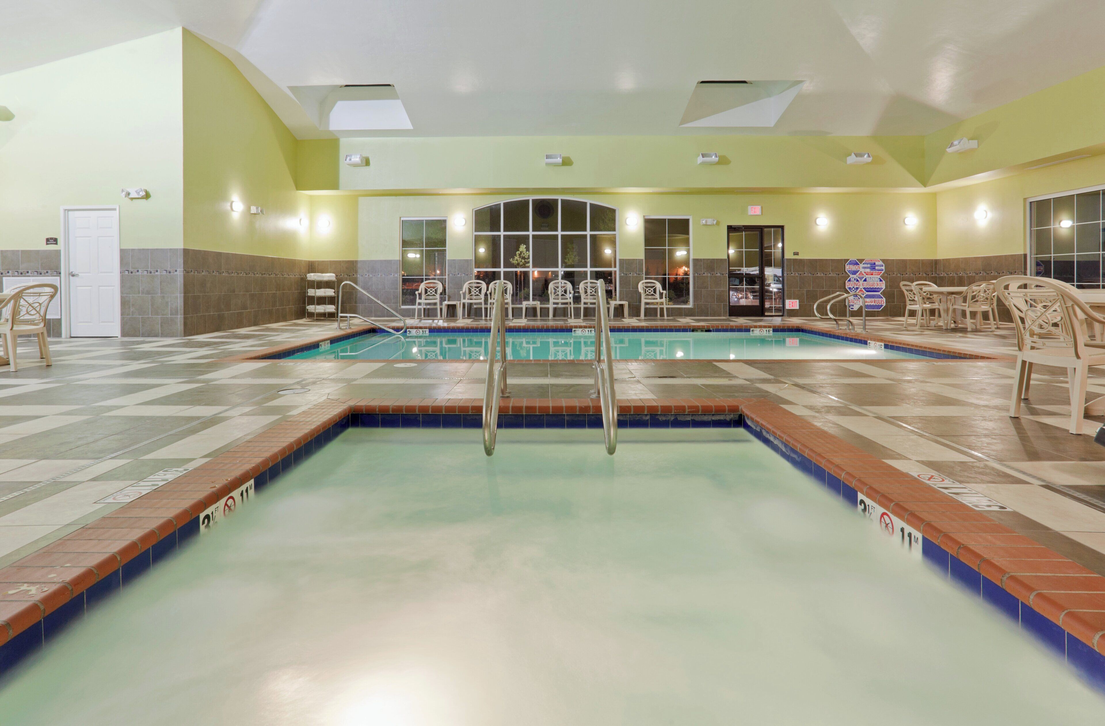 A hotel swimming pool with a diving board, lounge chairs, and a tiled floor.