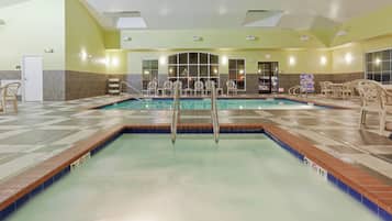A hotel swimming pool with a diving board, lounge chairs, and a tiled floor.