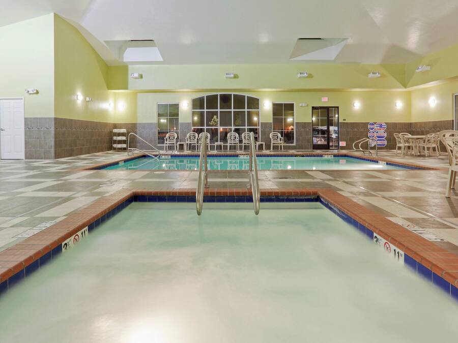 A hotel swimming pool with a diving board, lounge chairs, and a tiled floor.