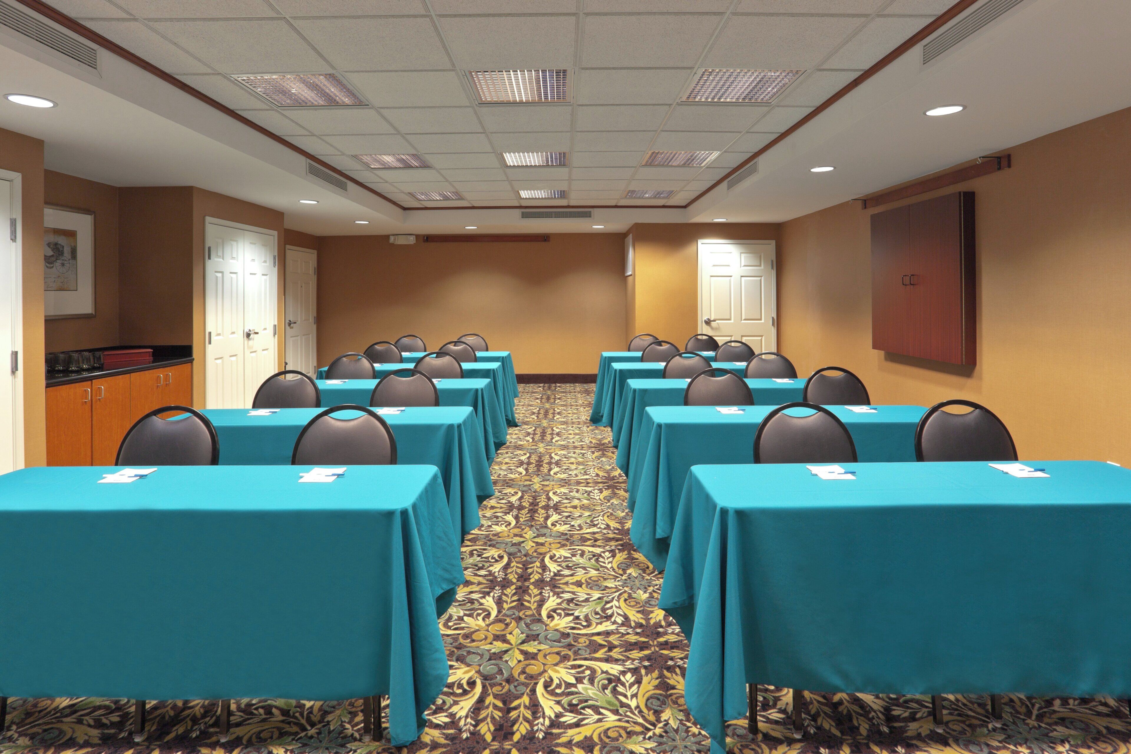A conference room with rows of tables and chairs, a patterned carpet, and a door on the left.