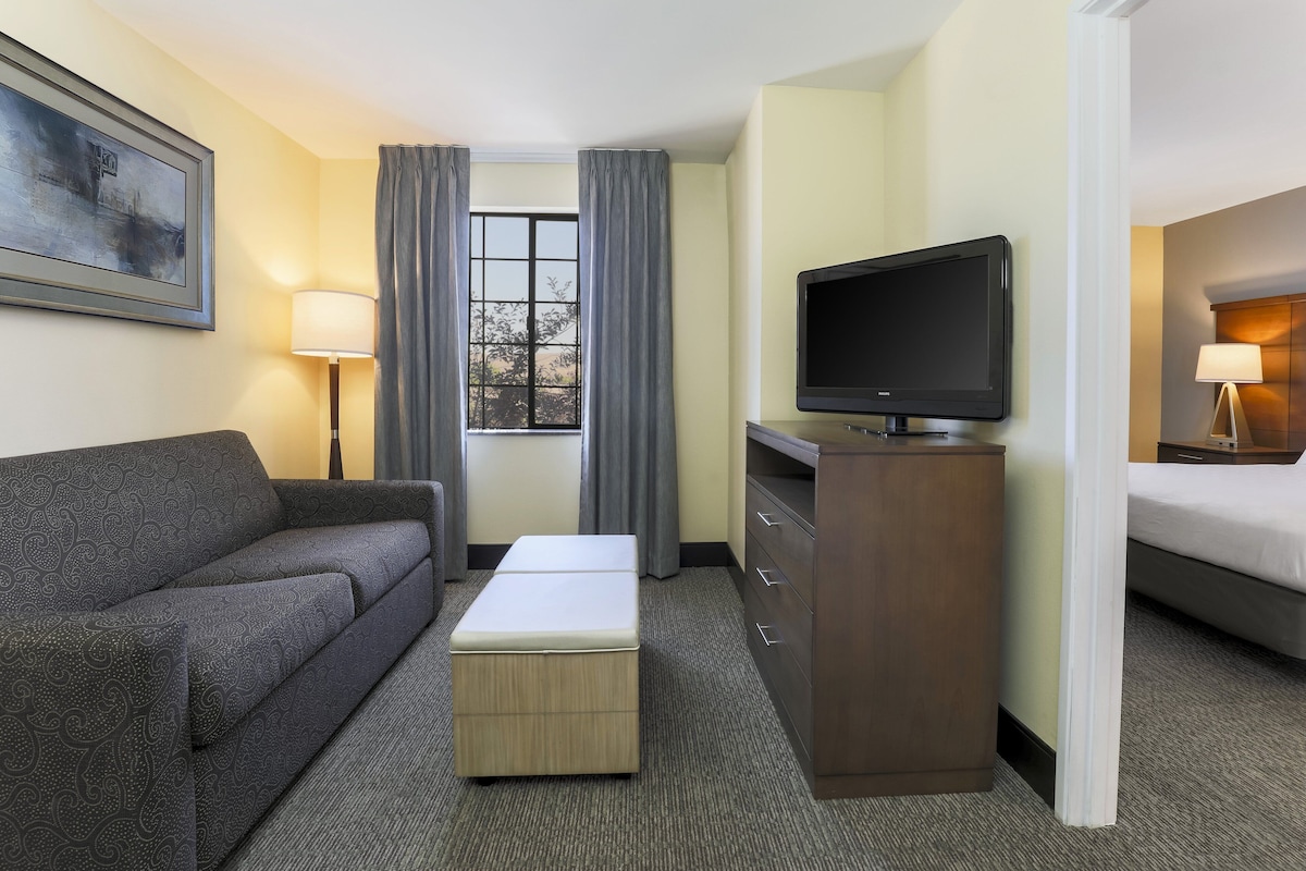 A hotel room with a sofa, a TV, a desk, a bed, and a window with curtains.