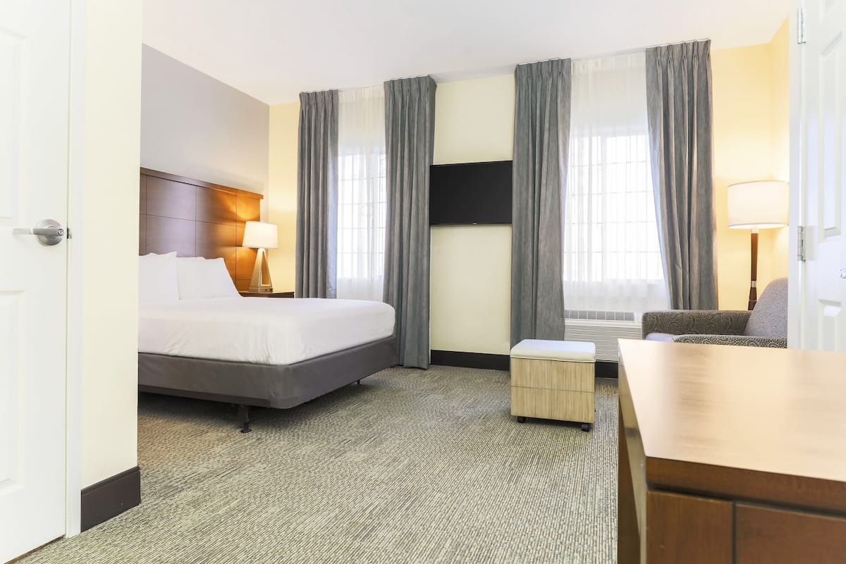 Ein Hotelzimmer mit Bett, Schreibtisch, Stuhl, Fernseher und einem Fenster mit Vorhängen.