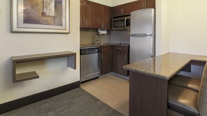 A modern kitchen with wooden cabinets, stainless steel appliances, a granite countertop, and a framed artwork on the wall.