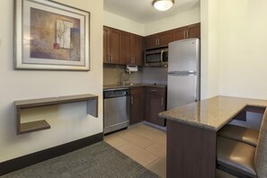 A modern kitchen with wooden cabinets, stainless steel appliances, a granite countertop, and a framed artwork on the wall.
