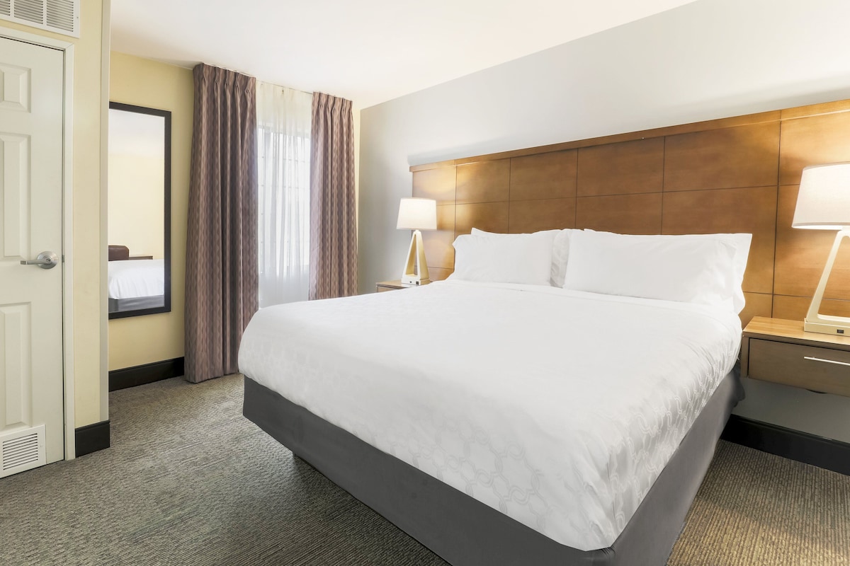 A hotel room with a large bed, a nightstand with a lamp, a wooden headboard, and a mirror on the wall.