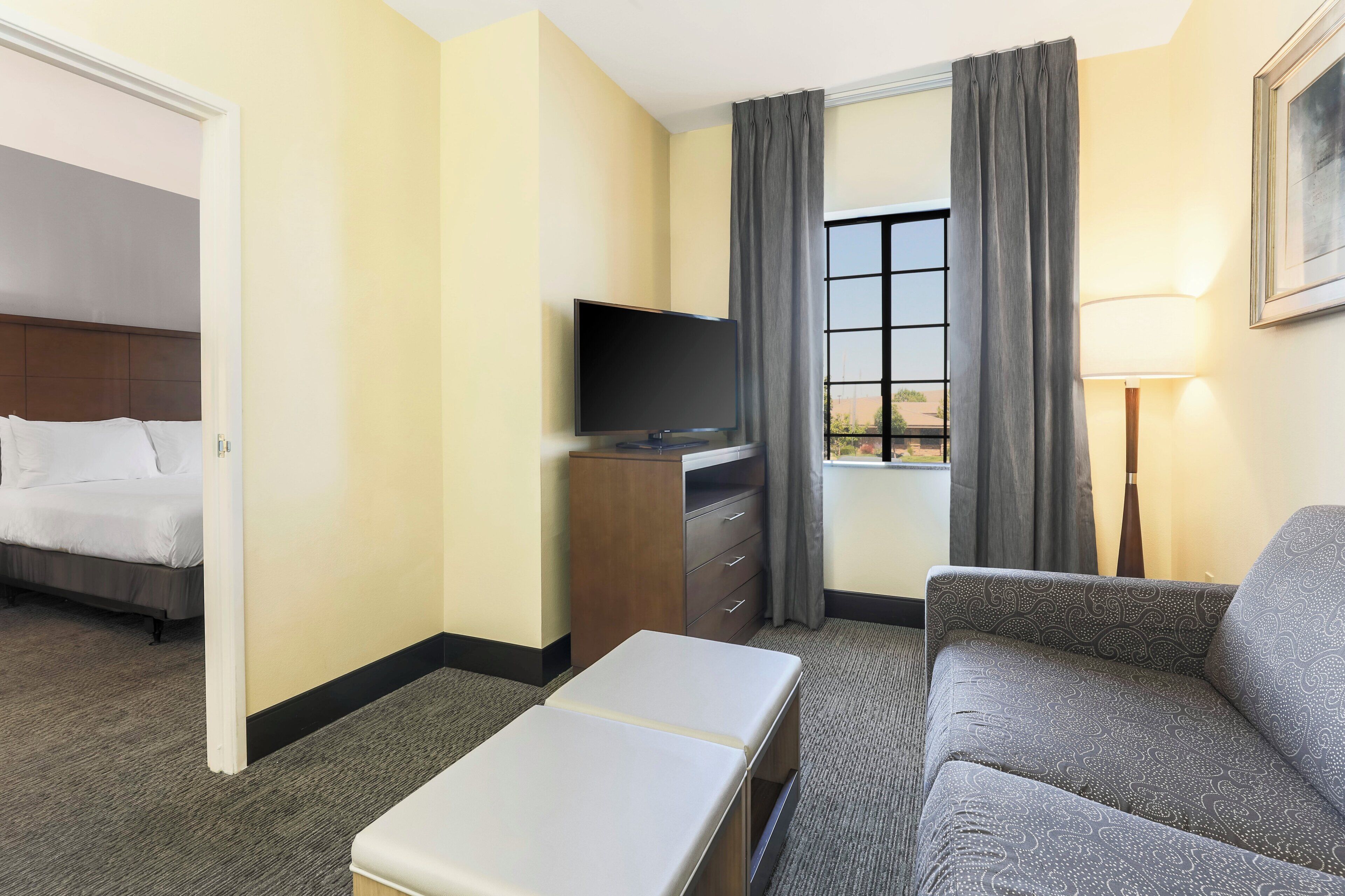 A hotel room with a bed, a TV, a sofa, a desk, and a window with curtains.