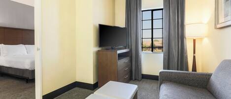 A hotel room with a bed, a TV, a sofa, a desk, and a window with curtains.