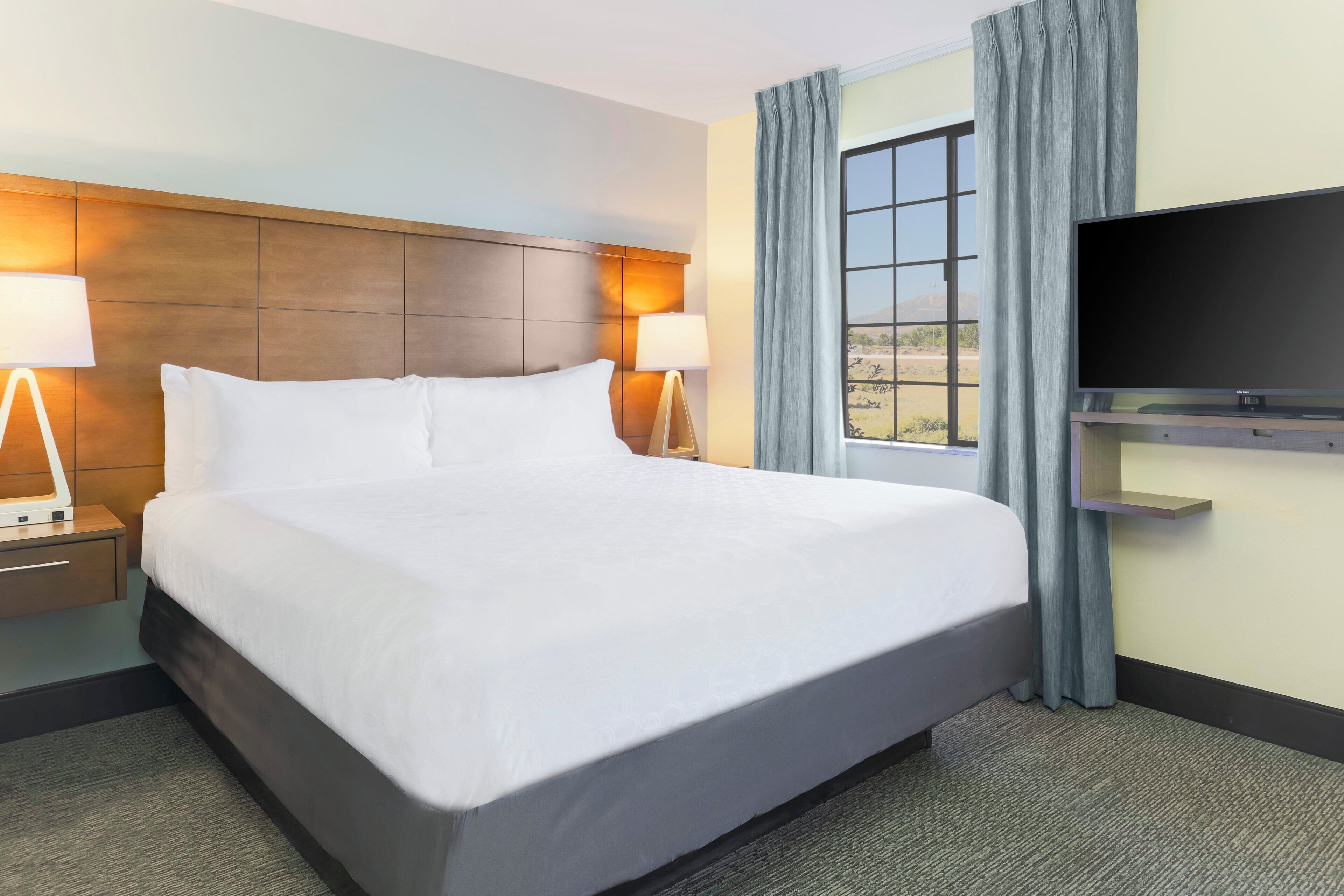 A hotel room with a large bed, bedside lamps, a flat-screen TV, and a window with curtains.