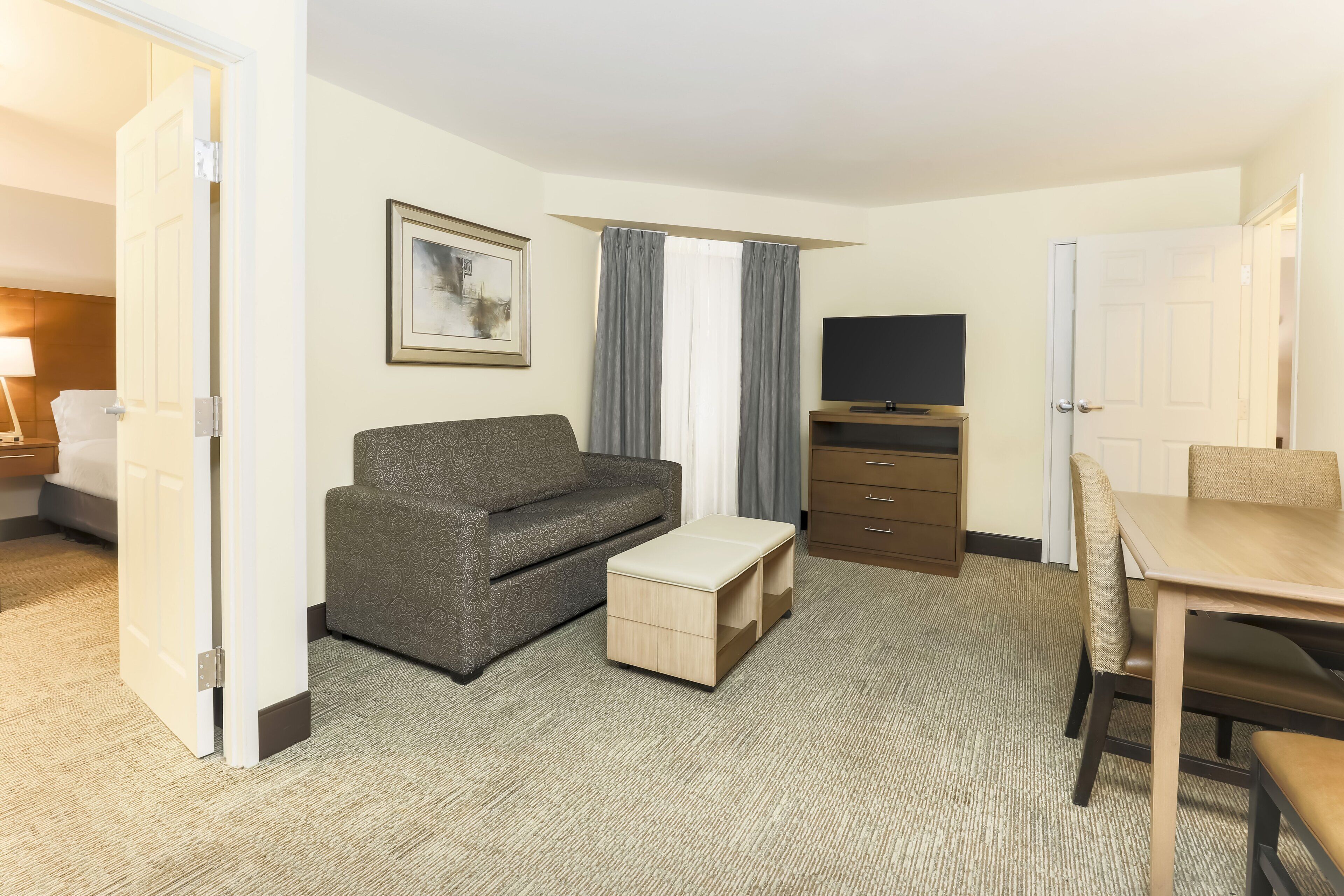 A hotel room with a sofa, a small table, a TV, and a desk with chairs.