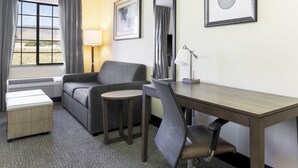 A hotel room with a sofa, a small table, a desk, a chair, a lamp, and a window with curtains.
