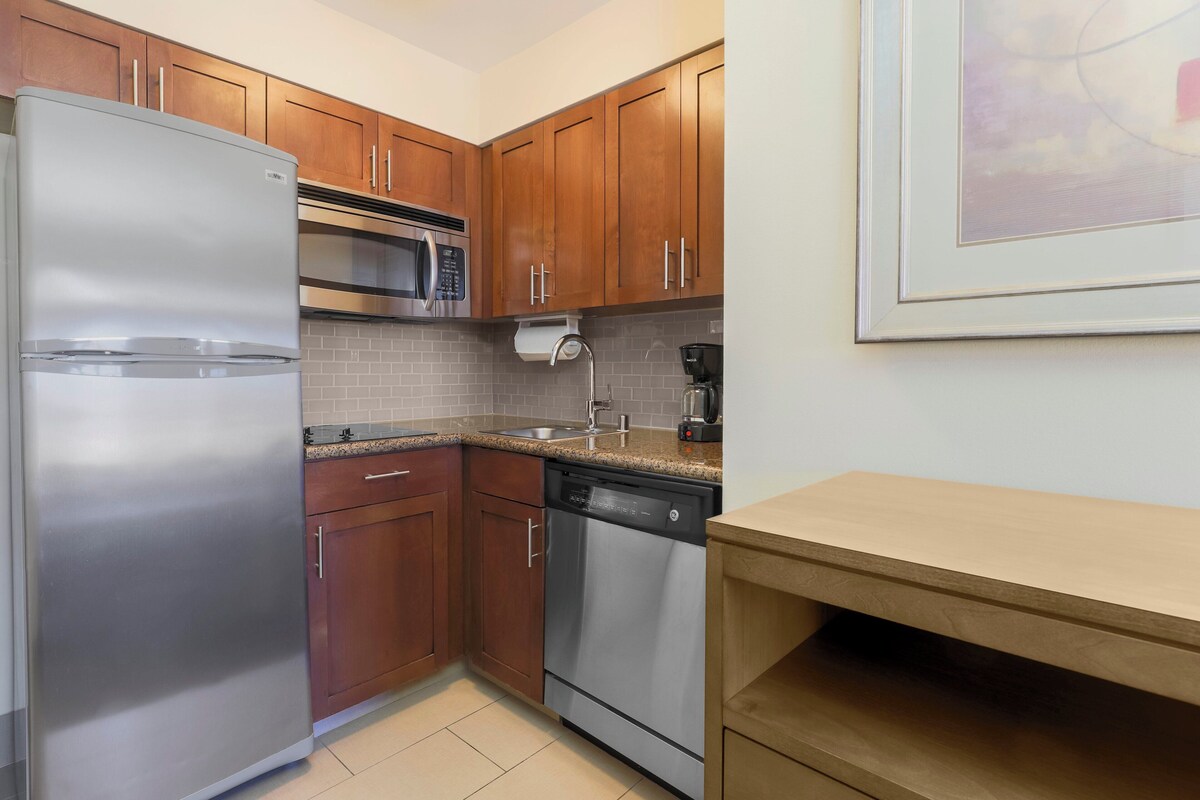 A compact kitchen with stainless steel appliances, wooden cabinets, and a countertop.