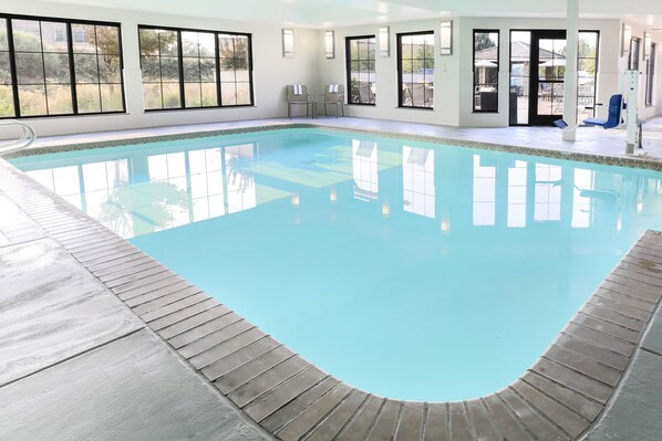 An indoor swimming pool with clear blue water, surrounded by large windows and a wooden deck.