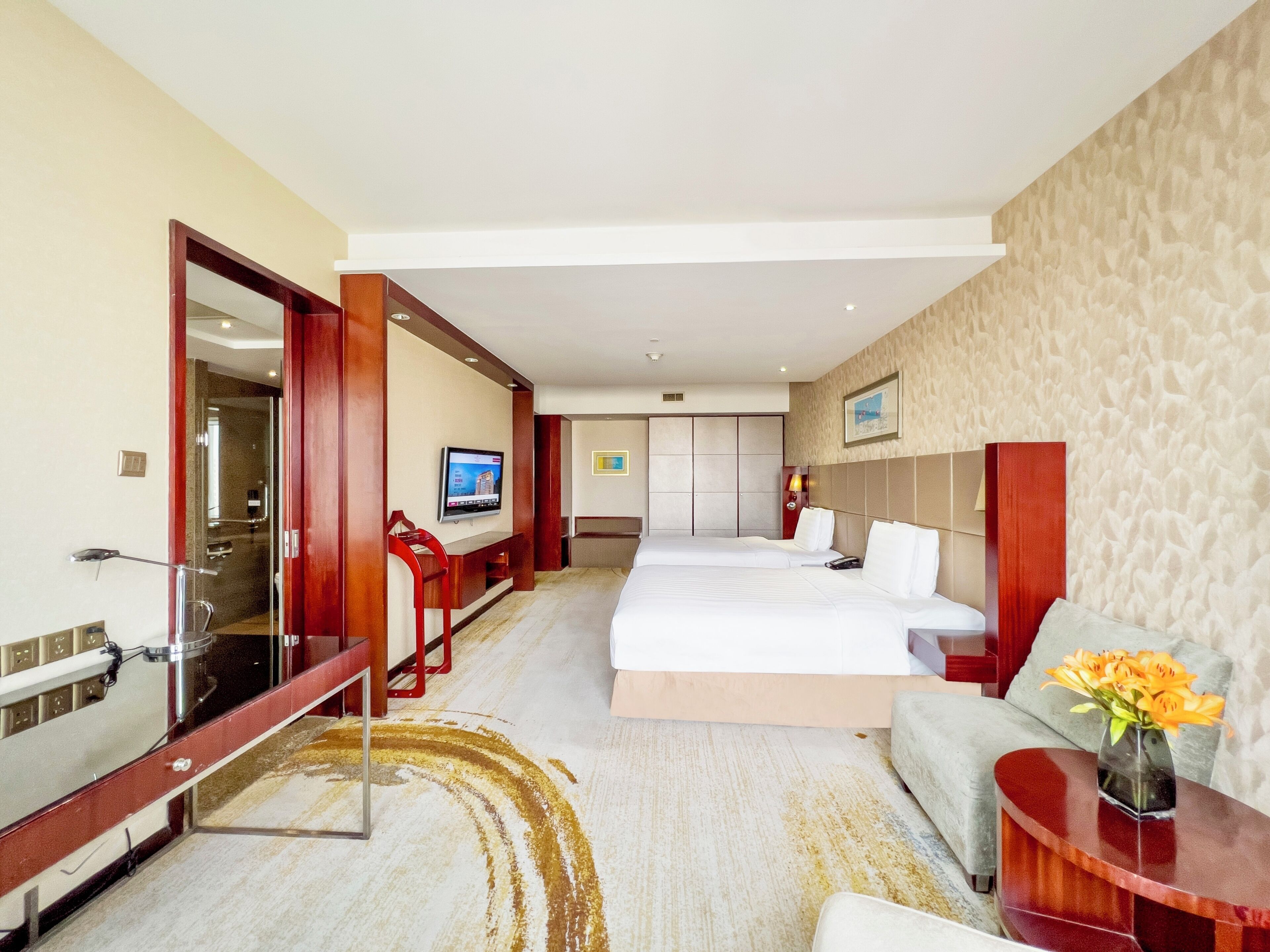 A hotel room with a large bed, a desk, a TV, and a bathroom visible through an open door.