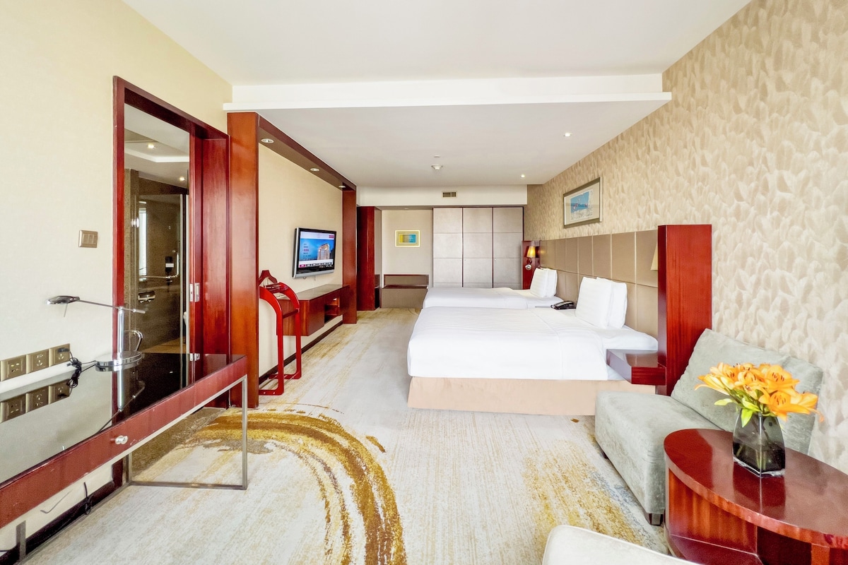 A hotel room with a large bed, a desk, a TV, and a bathroom visible through an open door.