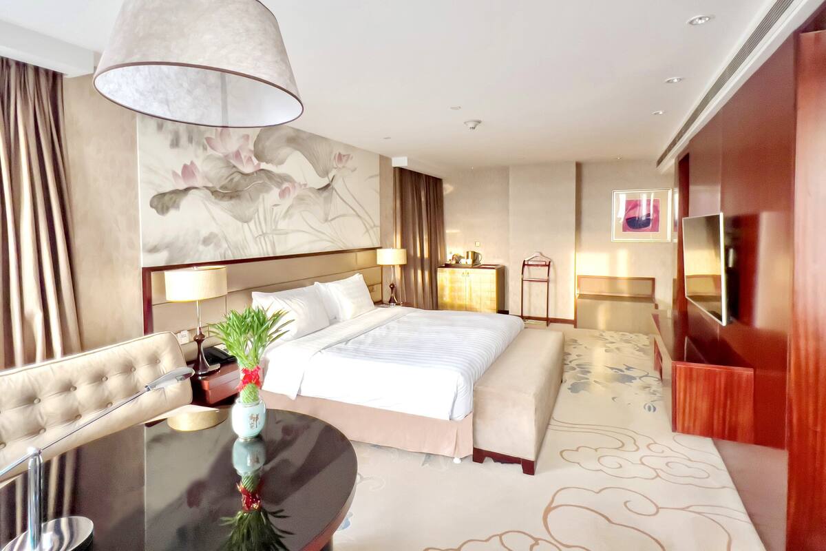 Ein modernes Hotelzimmer mit einem großen Bett, einem Esstisch, einem Fernseher und einer Wanddekoration.